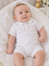 Baby in a white outfit sitting on a white textured surface