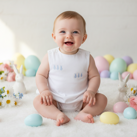 Baby sitting on a white surface with pastel Easter eggs and decorations in the background