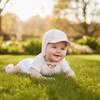 Baby lying on grass wearing a pink hat and white outfit