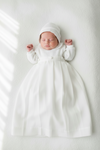 Newborn baby in a white gown and bonnet on a white background