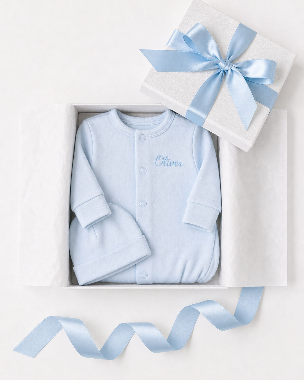Blue baby outfit with 'Oliver' embroidered, in a white box with a blue ribbon on a light gray background