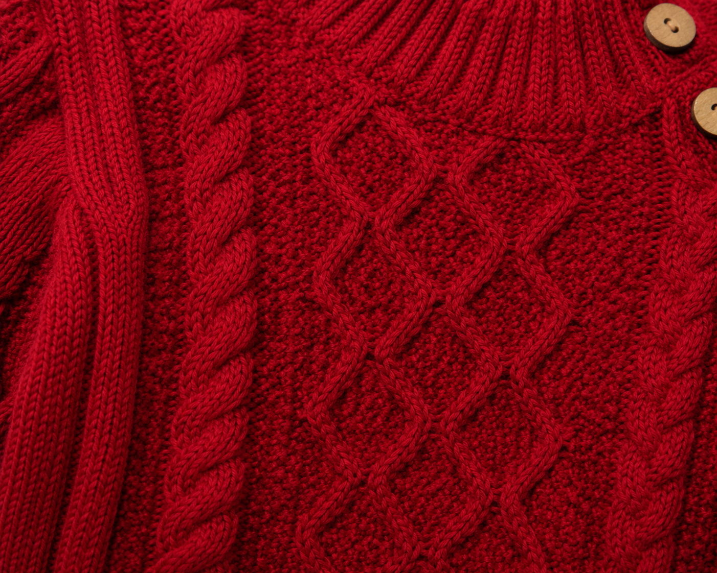 Close-up of a red knitted sweater with cable pattern and buttons.
