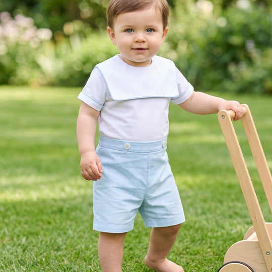 Carriage Boutique baby boy wearing a white and blue cotton bobby suit with a sailor collar standing on green grass