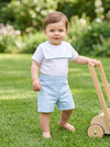 Carriage Boutique baby boy wearing a white and blue cotton bobby suit with a sailor collar standing on green grass