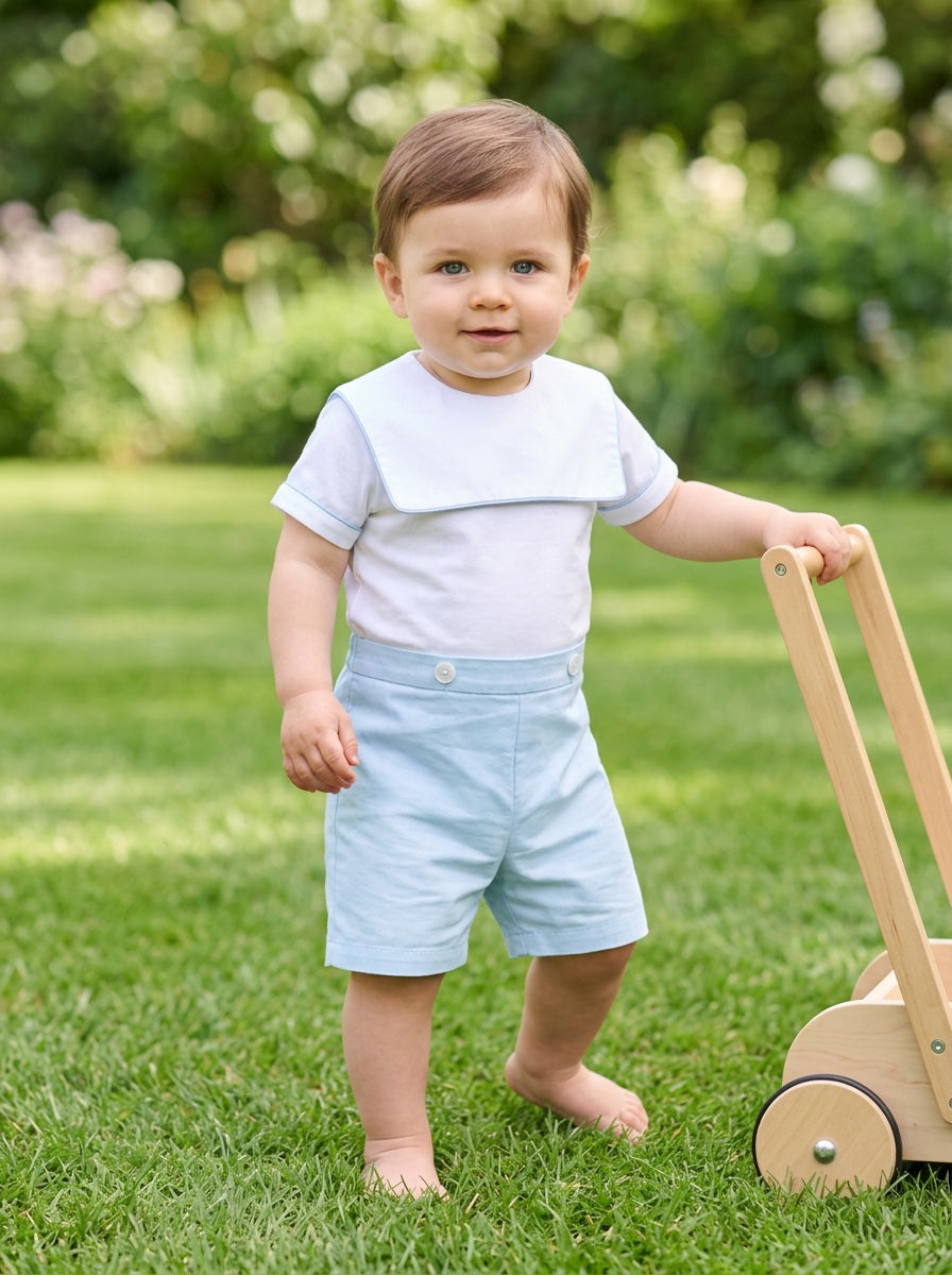 Carriage Boutique baby boy wearing a white and blue cotton bobby suit with a sailor collar standing on green grass