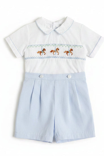 Children's white outfit with embroidered details on a wooden surface