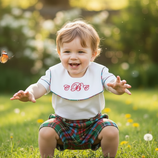 Child in a garden with a butterfly, wearing a bib with letters on it.