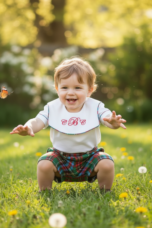Child in a garden with a butterfly, wearing a bib with letters on it.