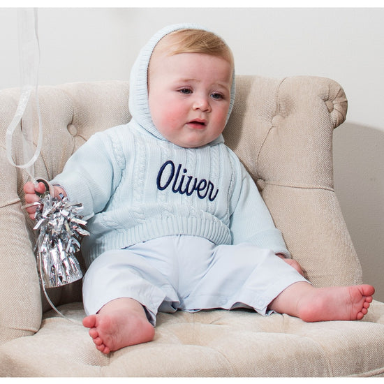 Carriage Boutique baby blue cable knit hooded sweater with navy blue Oliver embroidery, worn by a baby in a chair.