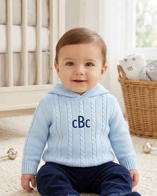 Carriage Boutique baby blue cable knit hooded sweater with navy monogram on chest worn by a smiling baby boy
