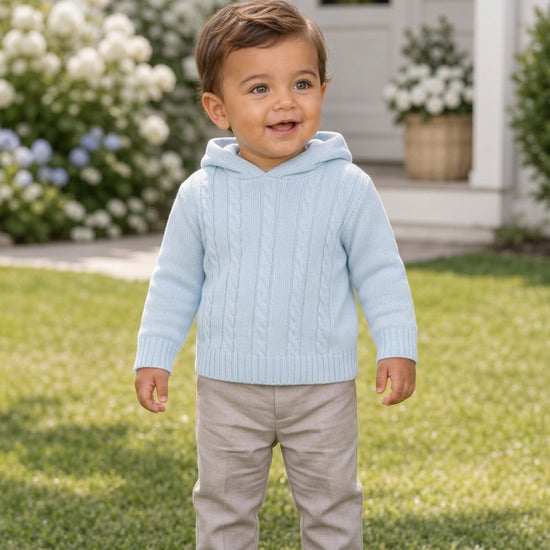 Carriage Boutique baby blue cable knit hooded sweater worn by a toddler standing on a green lawn.