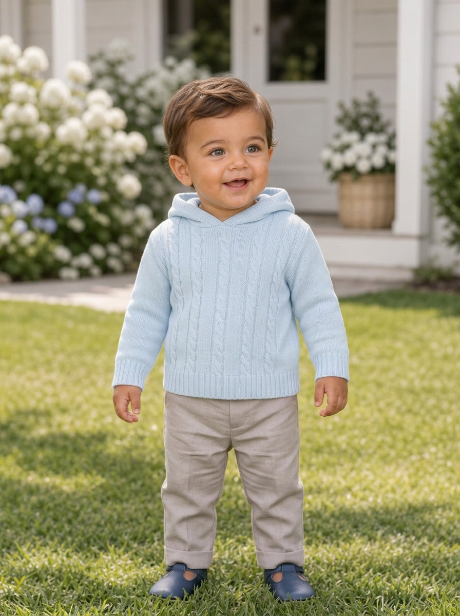 Carriage Boutique baby blue cable knit hooded sweater worn by a toddler standing on a green lawn.