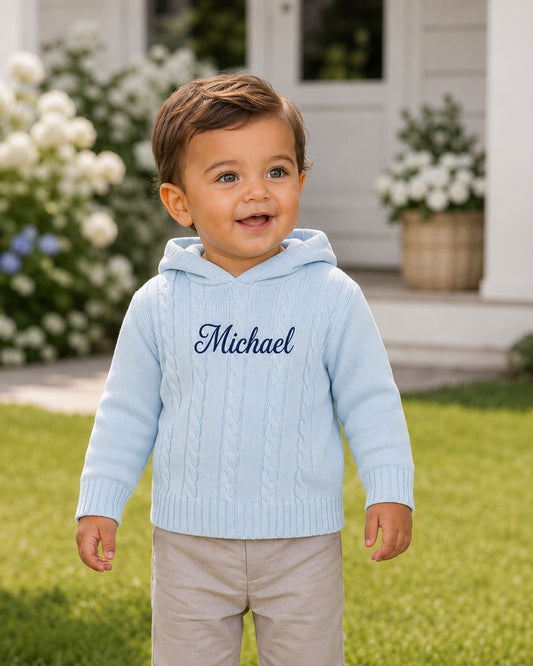 Carriage Boutique baby blue cable knit hooded sweater with custom monogram embroidery on a smiling toddler outdoors.