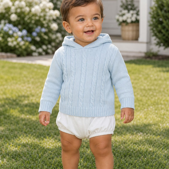 Carriage Boutique baby blue cable knit hooded sweater worn by a toddler standing on a green lawn.