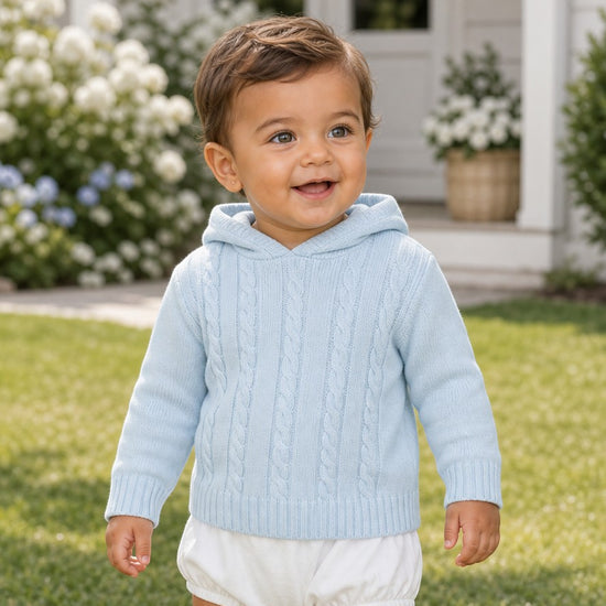 Carriage Boutique baby blue cable knit hooded sweater worn by a smiling toddler in a garden setting
