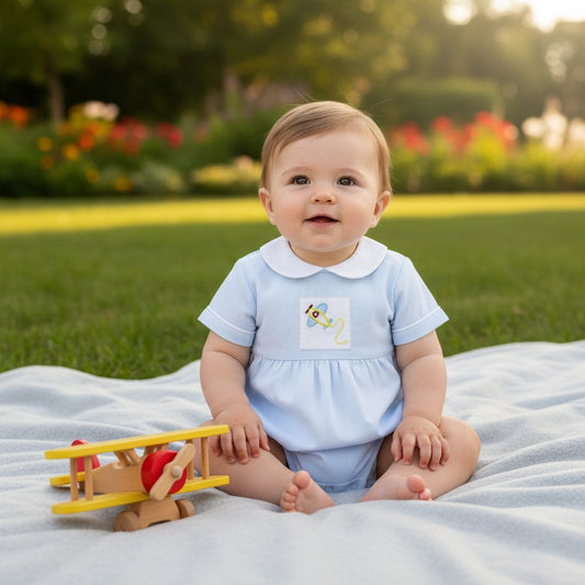 Carriage Boutique baby boy blue seersucker romper with white Peter Pan collar and embroidered airplane detail. 100% cotton.