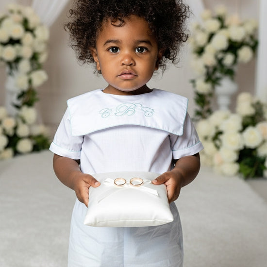 Child in a white outfit holding a small box with a ring in a decorated setting