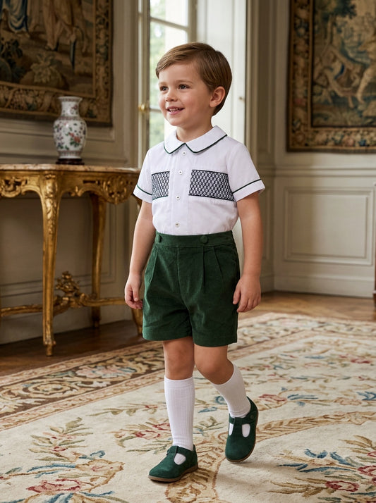 Carriage Boutique baby boy wearing a white smocked shirt and hunter green corduroy bobby suit shorts with white socks.