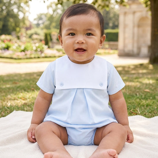 Carriage Boutique baby boy wearing a light blue cotton bubble romper with a white collar sitting on a park blanket