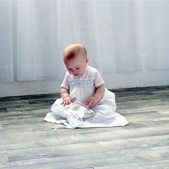 Carriage Boutique baby boy wearing a white christening gown with hand-smocked yoke and baby blue bullion cross design