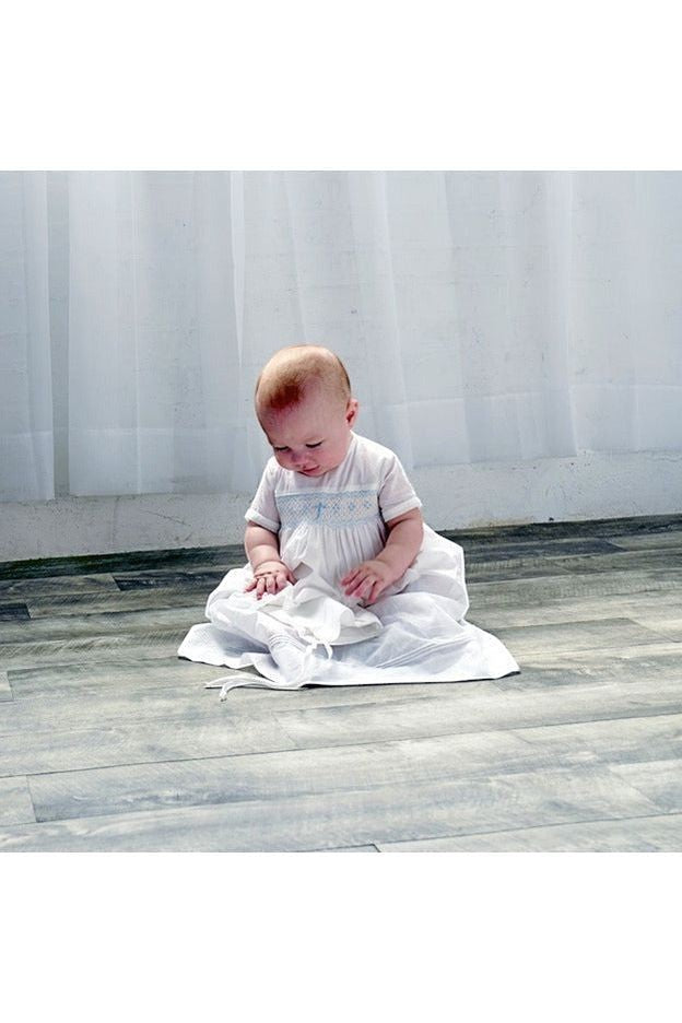 Carriage Boutique baby boy wearing a white christening gown with hand-smocked yoke and baby blue bullion cross design