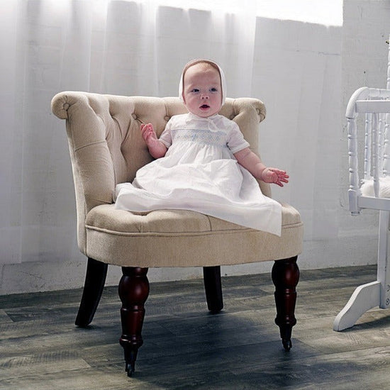 Baby boy wearing a Carriage Boutique white christening gown with hand-smocked blue cross yoke and matching bonnet