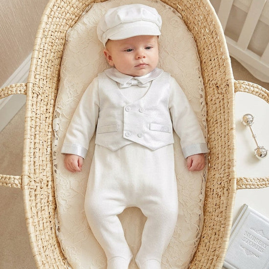 Carriage Boutique baby boy christening footsie with silk vest and matching cap lying in a woven moses basket.