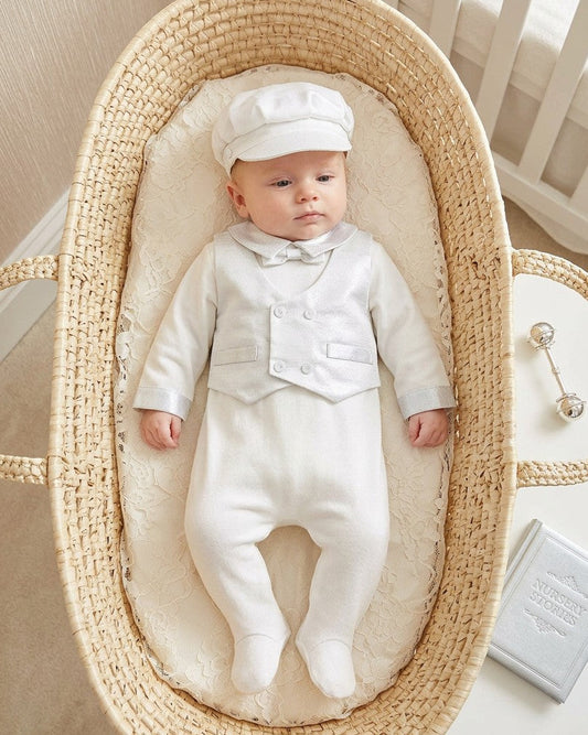 Carriage Boutique baby boy christening footsie with silk vest and matching cap lying in a woven moses basket.