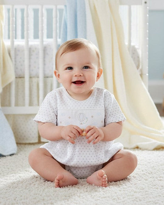 Carriage Boutique baby boy wearing a white cotton bubble romper with hot air balloon smocking and grey polka dots