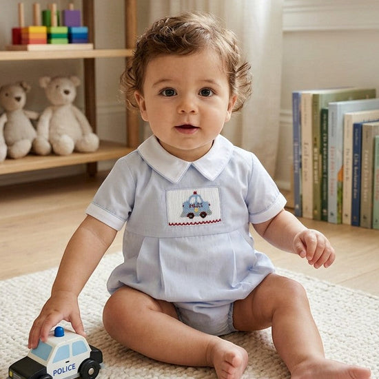 Carriage Boutique baby boy bubble romper in light blue cotton with hand-smocked police car embroidery and white collar