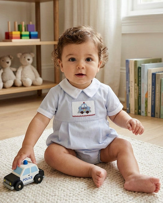 Carriage Boutique baby boy bubble romper in light blue cotton with hand-smocked police car embroidery and white collar