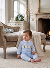 Carriage Boutique baby boy wearing a light blue longall with smocked Christmas tree embroidery in a festive room