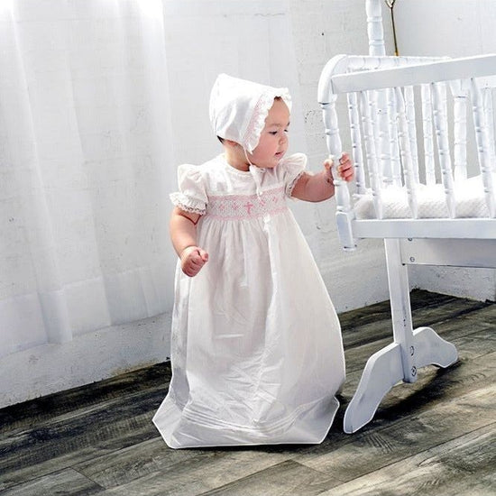 Carriage Boutique baby girl christening gown with pink bullion cross embroidery, smocked yoke, and matching ruffled bonnet