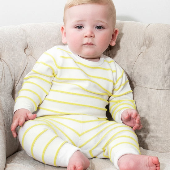 Baby wearing a Carriage Boutique white and yellow striped long-sleeve cotton knit legging set while sitting in a chair