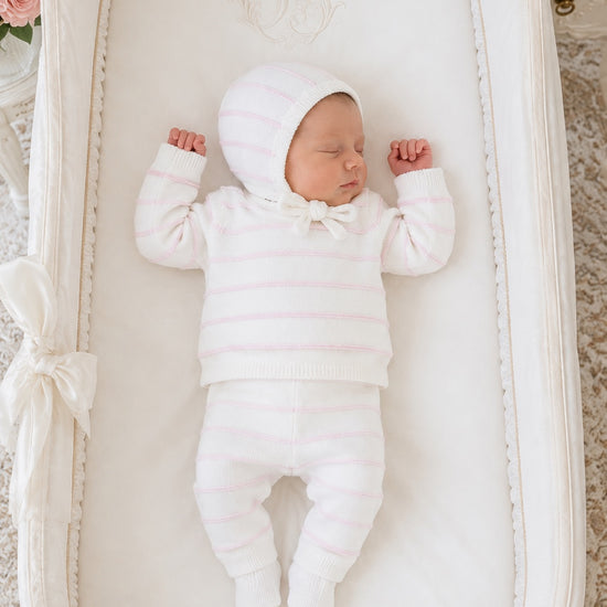Newborn baby sleeping in a Carriage Boutique white knit legging set with blush pink stripes and matching bonnet