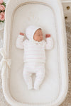 Newborn baby sleeping in a Carriage Boutique white knit legging set with blush pink stripes and matching bonnet