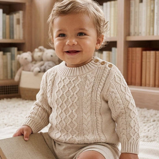 Carriage Boutique baby boy wearing a cream fisherman knit cotton pullover sweater with shoulder button details.