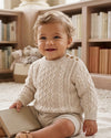 Carriage Boutique baby boy wearing a cream fisherman knit cotton pullover sweater with shoulder button details.