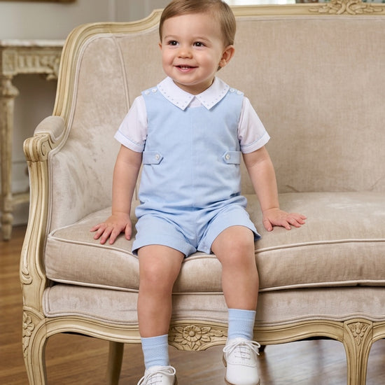 Carriage Boutique baby boy wearing a light blue cotton shortall romper with a white collared shirt and matching socks