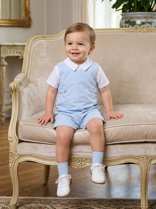 Carriage Boutique baby boy wearing a light blue cotton shortall romper with a white collared shirt and matching socks