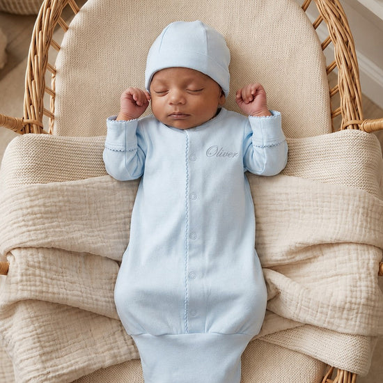 Carriage Boutique blue newborn sleep sack with matching hat and scalloped trim, worn by a sleeping baby in a basket.
