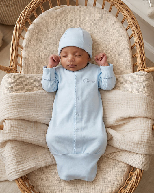 Carriage Boutique blue newborn sleep sack with matching hat and scalloped trim, worn by a sleeping baby in a basket.