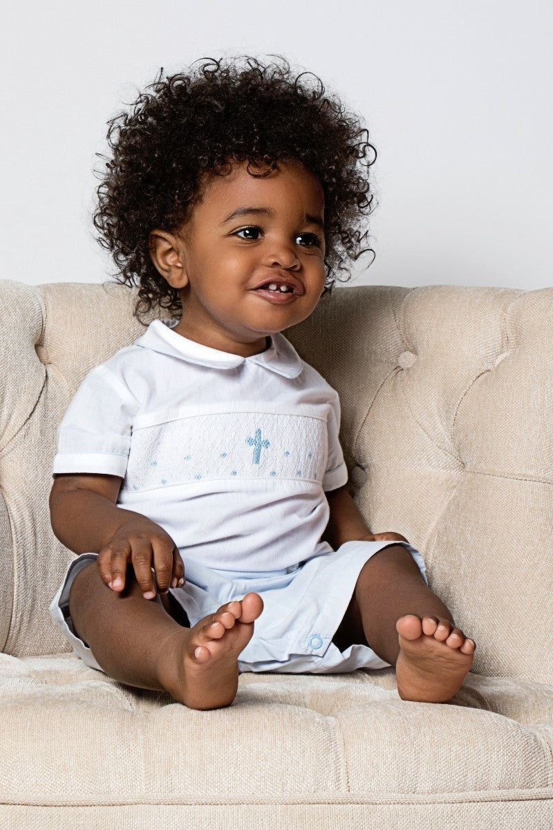 Carriage Boutique baby boy's light blue smocked christening bobbie suit with blue cross embroidery and Peter Pan collar.