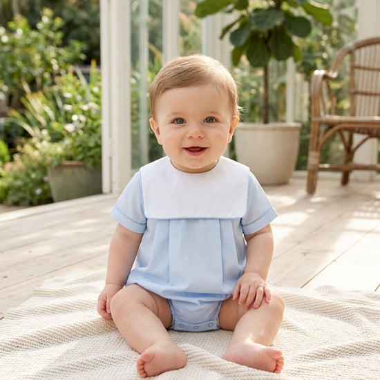 Carriage Boutique baby boy wearing a light blue cotton romper with a white collar, sitting on a textured blanket.