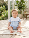 Carriage Boutique baby boy wearing a light blue cotton romper with a white collar, sitting on a textured blanket.