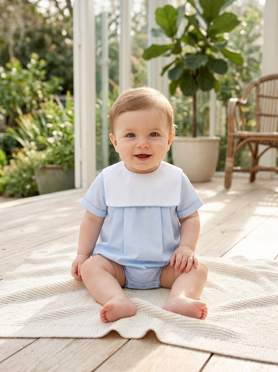 Carriage Boutique baby boy wearing a light blue cotton romper with a white collar, sitting on a textured blanket.
