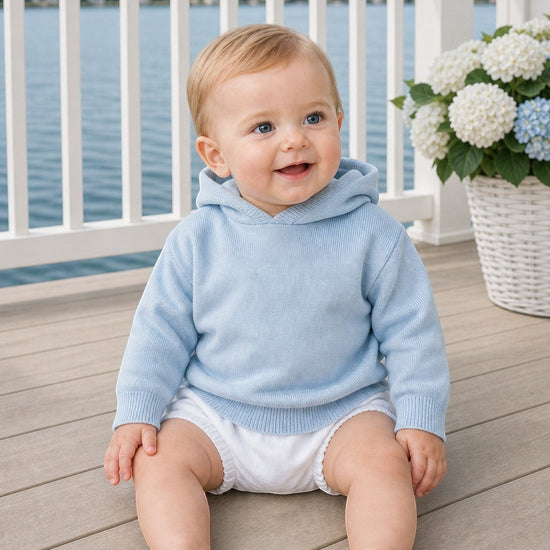 Carriage Boutique baby boy wearing a soft blue cotton hooded sweater with a zip back detail on a wooden deck.