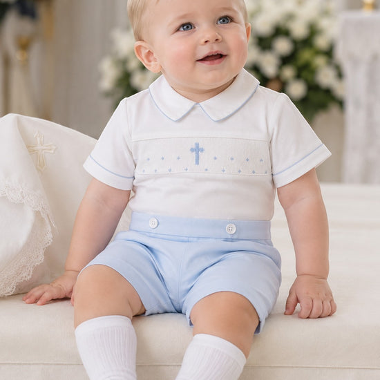 Carriage Boutique white cotton bobbie suit with blue smocking, cross detail, and light blue shorts for baby boys.
