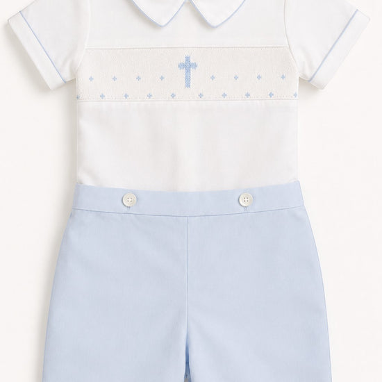 Carriage Boutique white short-sleeve bobbie suit with blue smocking, cross detail, and light blue shorts. Cotton.