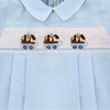 Carriage Boutique light blue cotton baby boy romper with hand-smocked white panel featuring brown dogs in blue wagons.